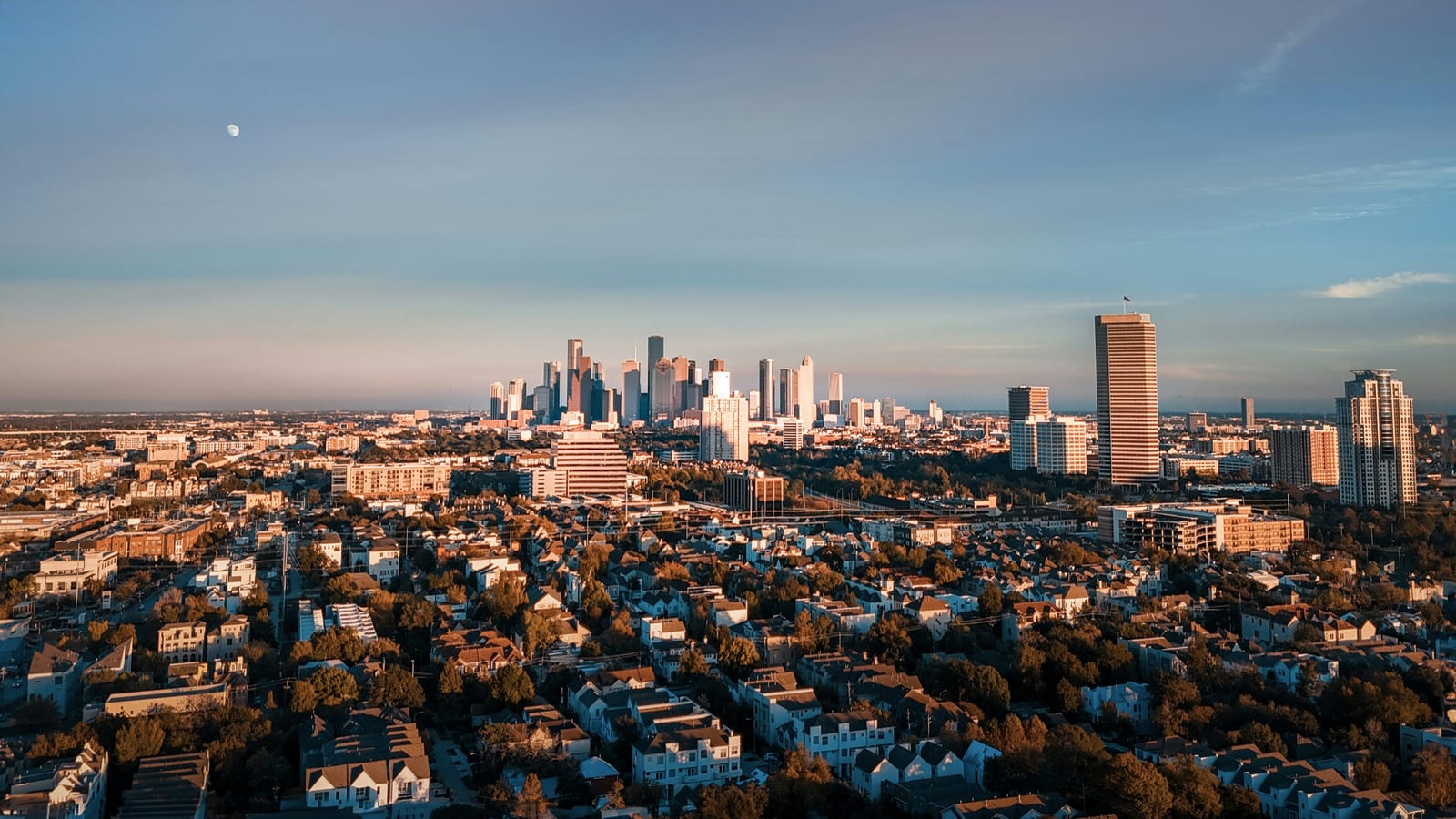 The Houston skyline seen from the air in evening light, the moon above it.