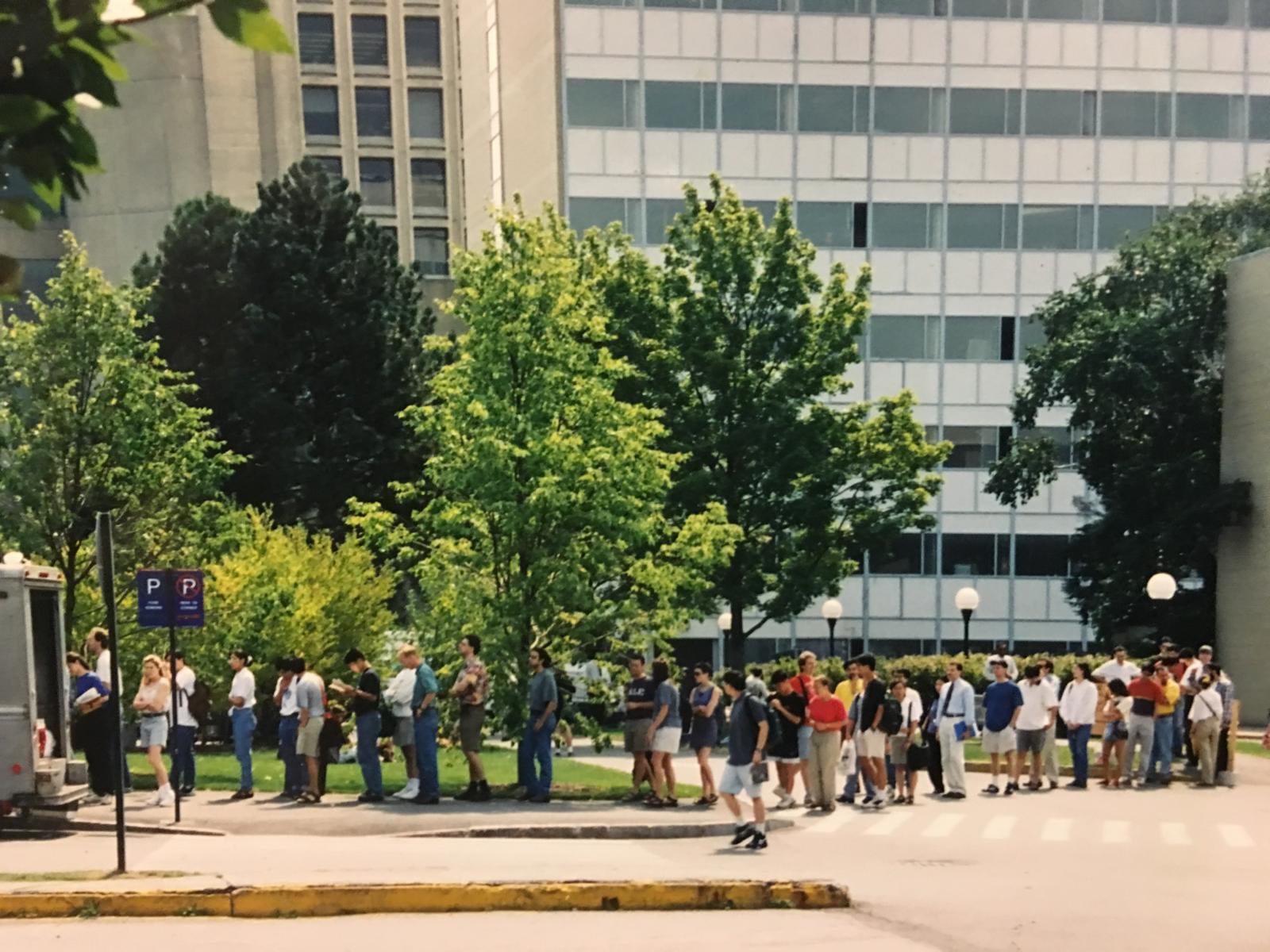 A long line of students waiting on a footpath outside Building 66 at MIT on a summer day in the mid 1990s.