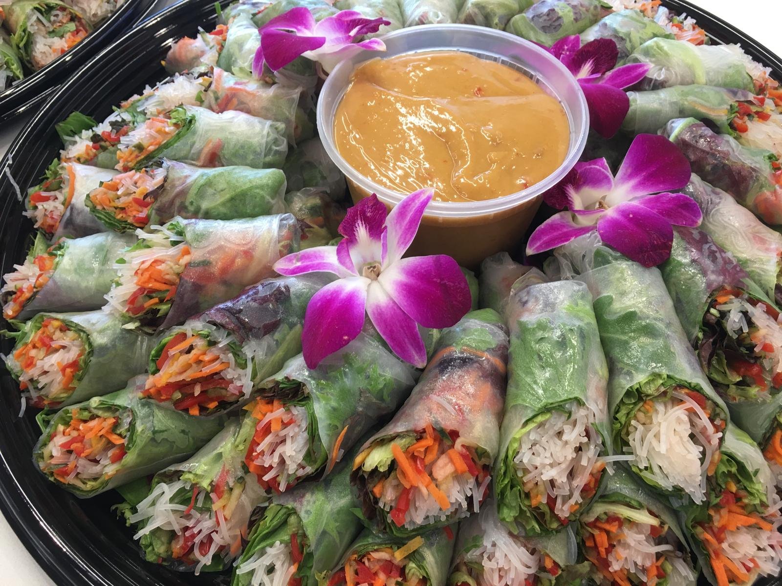 Spring rolls arranged around a peanut dipping sauce, garnished with orchids.