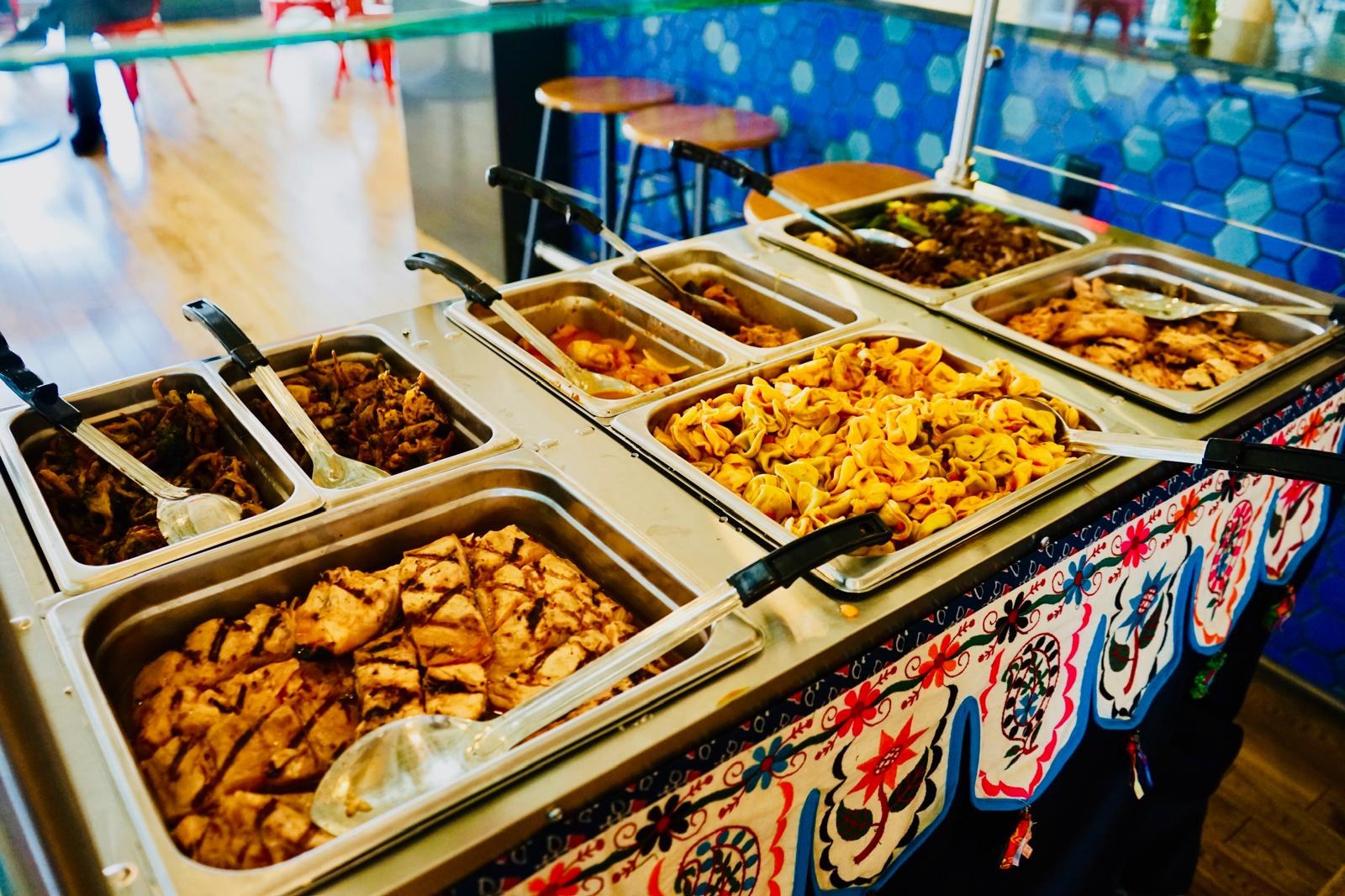Chafing dishes of noodles, chicken and vegetables along a catering table.